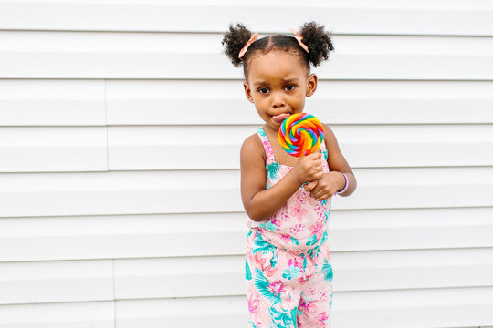 A little girl with pigtails enjoying her rainbow colored lollipop
