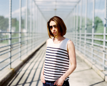 Portrait of a beautiful and fashionable woman standing on a fenced overpass