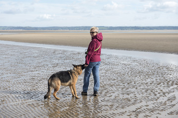 Mature woman walking on the beach with her Alsatian dog  