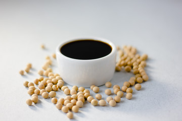 Soybean sauce surrounded by soy beans over white background.