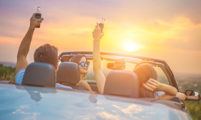The happy people sit in a cabrio on the bright sun background