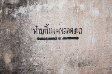 Painted on Dirty Concrete Wall in Thai Language means " Please Do Not Litter This Area " and Black arrow show area