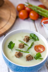 Beautiful asparagus cream soup with toasted bread on white wooden table.