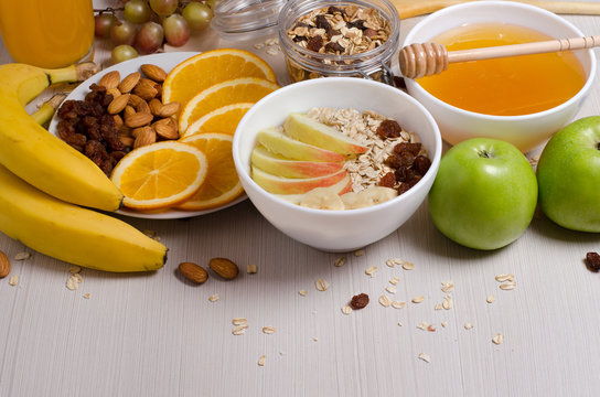 Healthy food. Fruit, homemade granola, nuts, oatmeal, honey, orange juice on a white table.
