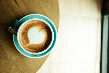 top view. cup with coffee has a heart shape on top both placed on wood table and sunshine are background. image for coffee art, beverage, drink, food, art concept