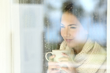 Girl looking through a window holding coffee in winter