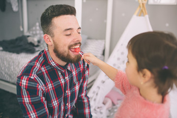 Cute little daughter and her handsome young dad iare playing together in child's room. Dady and child spend time together while sitting on the floor in bedroom