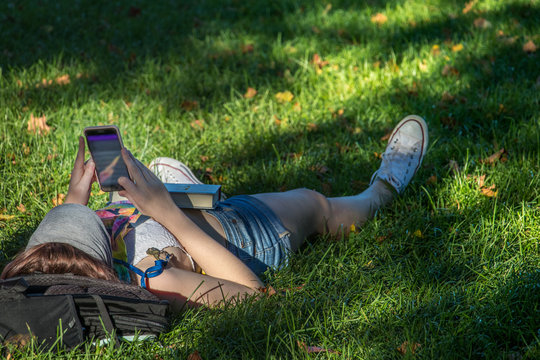 Young woman lying on the grass is browsing her cellphone