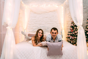 happy woman and man on a background of New Year's Christmas decor smiling in bed