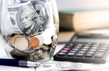 Fototapeta premium Coins, calculator and banknote in a glass jar on the textbook.
