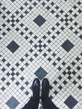 Looking Down On Person Wearing Black Boots Standing On A Black And White Tiled Floor