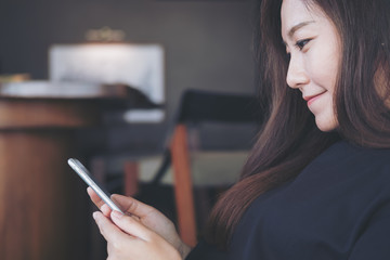 Closeup image of a beautiful Asian woman with smiley face using and looking at smart phone in modern cafe