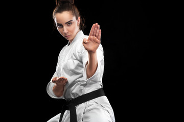 Sporty karate and taekwondo woman in white kimono with black belt on dark background. Sport concept...