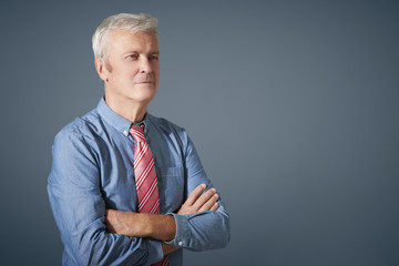 Portrait of a confident senior businessman standing against isolated dark grey background. Copy space.