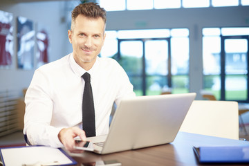 Fototapeta premium Businessman working at the office. Shot of a middle aged businessman using his mobile phone and laptop while working at the office. 