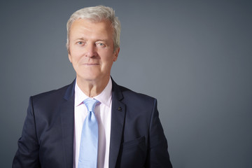 Portrait of a confident senior businessman standing against isolated dark grey background. Copy space.