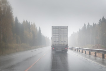 Big rig semi truck with refrigerator unit on reefer trailer transports commercial industrial cargo on a multi-lines highway with wet shiny coating and rain dust in rainy weather. - 176892787