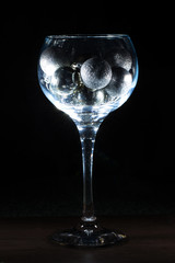 Wine glass filled with Christmas balls. On a black background.