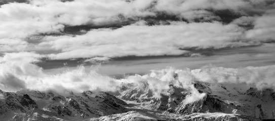 Black and white panoramic view on snow mountains and sunlight cloudy sky at winter evening
