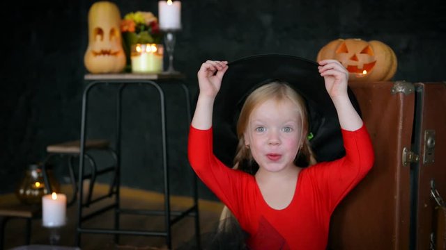 A little girl, a witch, in a hat, eats sweets and scares the camera.