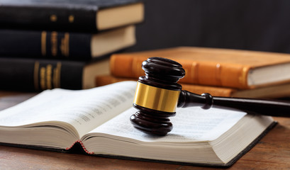 Judge gavel on an open book, wooden desk, law books background