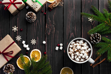 Obraz na płótnie Canvas A cup of hot coffee with marshmallow, spruce branches, cones, Christmas gifts, mugs of orange, snowflakes, cinnamon. Traditional festive decoration Christmas dark background top view.