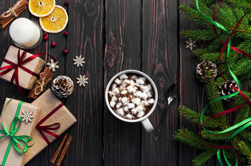 A cup of hot coffee with marshmallow, spruce branches, cones, Christmas gifts, mugs of orange, snowflakes, cinnamon. Traditional festive decoration Christmas dark background top view.