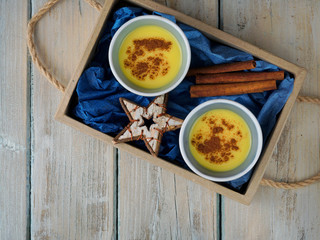 Homemade eggnog in two cups, cinamon and  Christmas decoration in paper box on wooden table,