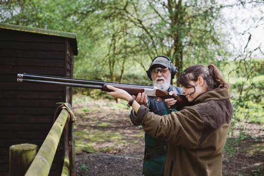 Young girl learning to fire a shoot gun in a firing range with an instructor .