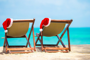 Fototapeta premium Sun loungers with Santa Hat at beautiful tropical beach with white sand and turquoise water. Perfect Christmas vacation