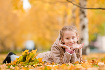 Portrait of adorable little girl with yellow leaves bouquet in fall. Beautiful smiling kid lying on leaves carpet