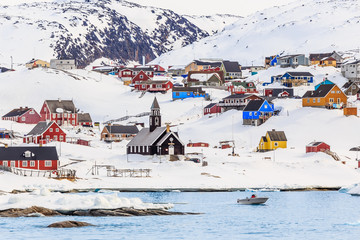 Arctic settlement with colorful Inuit houses on the rocky hills covered in snow with snow and mountain in the background, Ilulissat, Greenland