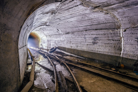 Bifurcation of rusty narrow-gauge railway. Tunnel in abandoned mine. Turn the tunnel. Light from the turn. 