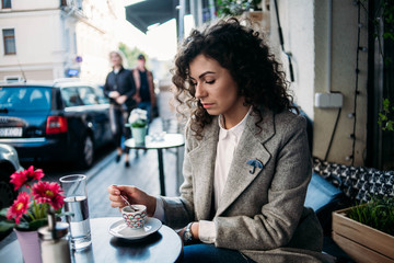 a girl drinks coffee on the summer terrace of a cafe, stirs a cappuccino,