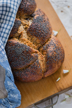 Overhead view of plaited bread with poppy seeds on a breadboard