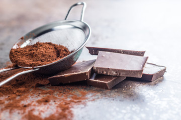 Dark cocoa powder in a sieve and chocolate.