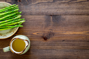Cooking fresh asparagus. Greens on plate near a jug of oil on dark wooden background top view copyspace