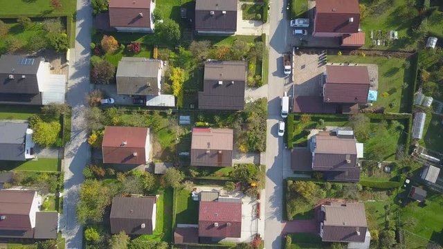 AERIAL TOP DOWN Flying over red rooftops in idyllic suburban town on sunny autumn day. Row houses with green garden lawns and narrow empty roads in peaceful suburbia. Perfect homes in quiet suburbia
