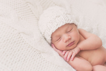 Beautiful newborn baby sleeping peacefully on a white blanket wearing a matching hat