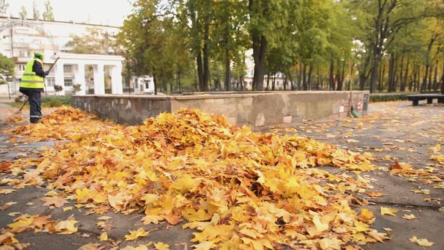 Female janitor in uniform sweeping fallen leaves in park, low-paid job, crisis