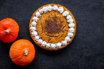 Obraz na płótnie Canvas Homemade pumpkin pie decorated whipped cream and chocolate near pumpkins on black background top view copyspace
