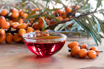 Sea buckthorn oil in a glass bowl with sea buckthorn branches