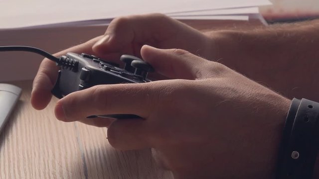 Man playing computer video game in the office. Close up of male hands holding a joystick controller, having fun with electronic games. Gaming, entertainment and technology concept.