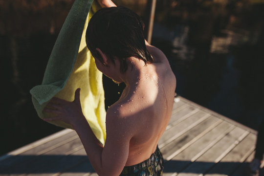 Young, wet boy drying off with towel after jumping the lake