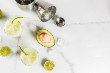 Alcoholic cocktail recipes and ideas. Avocado and lime margarita with salt, on a white marble kitchen table. Copy space top view