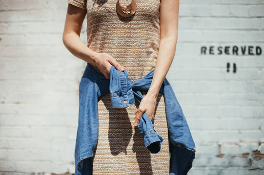 Girl tying denim shirt around her waist with brick wall background