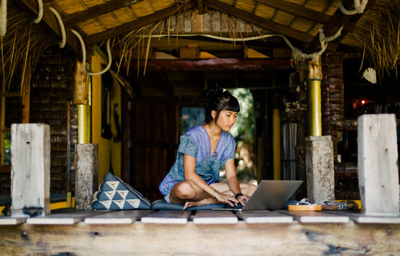 Casual young woman working on laptop in tropical house