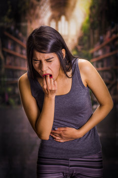 Beautiful and lonely girl suffering of anorexy, holding her stomach and putting his fingers in her mouth to induce to vomit, a blurred background