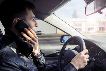 Young man speaking on the mobile phone while driving a car. Danger on the road, drive with caution