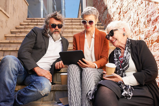 Three old friends enjoying the sun on the steps using digital tablet technology